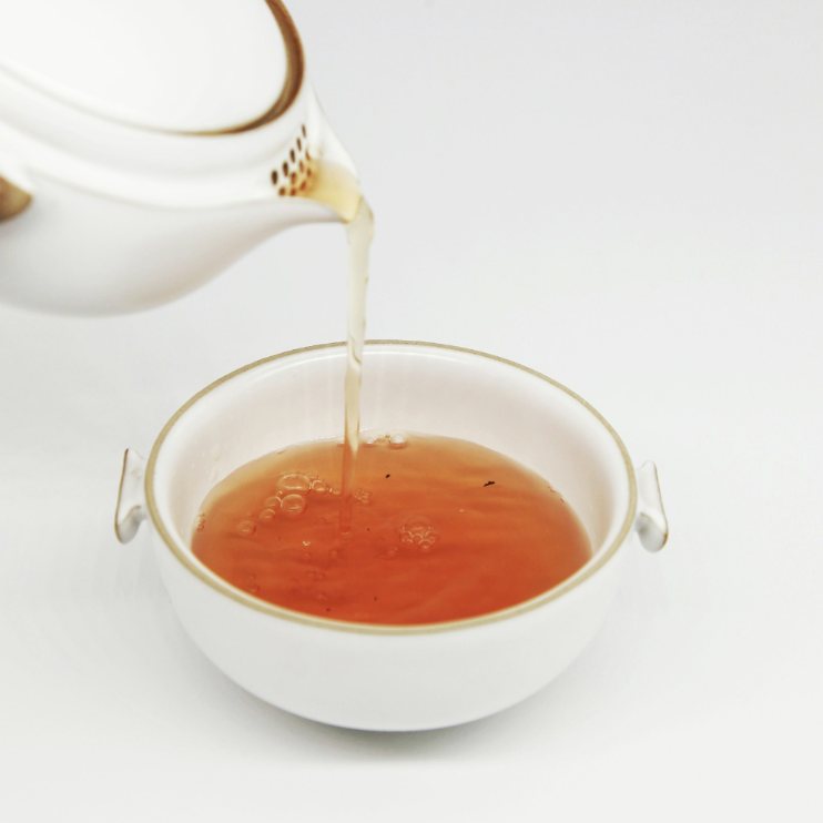 Tisana versata da una teiera bianca in una tazza